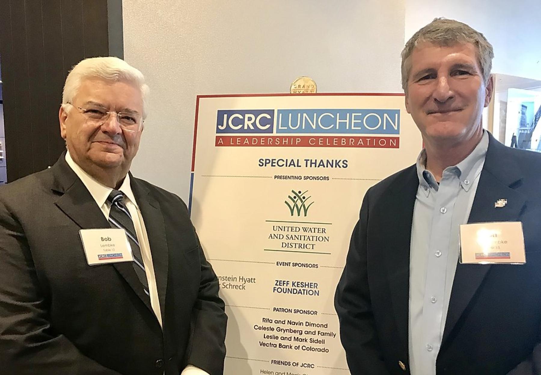 Bob Lembke, President of United Water and Sanitation District, and Ron vonLembke, Chief of Staff of United Water, pose in front of the JCRC Sponsorship Recognition Banner. United Water and Sanitation District and Bob Lembke, personally, helped sponsor the luncheon. (Photo by Lynn Bartels)