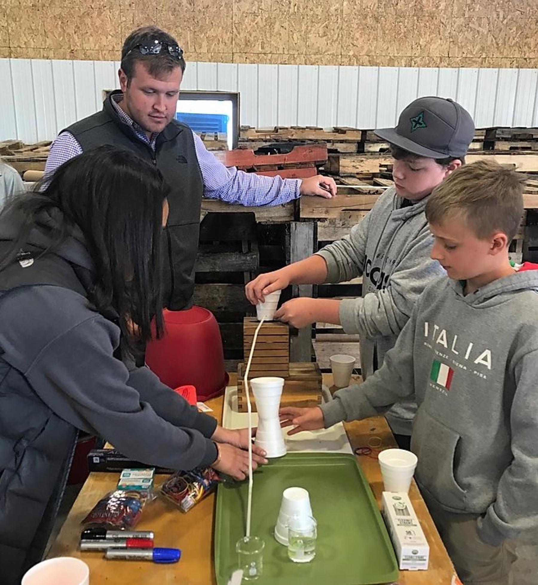 From clockwise, Colorado State University students Muriel Butler and Jordan Campbell assist Jaxon Sullivan, 12, who attends Weber Middle School in Fort Collins, and Jacob Grifware, 11, who was visiting from Grand Junction. Their water experiment involved straws, a beaker and a cup.  They attended an open house Oct. 5 sponsored by the Subsurface Irrigation Efficiency Project.